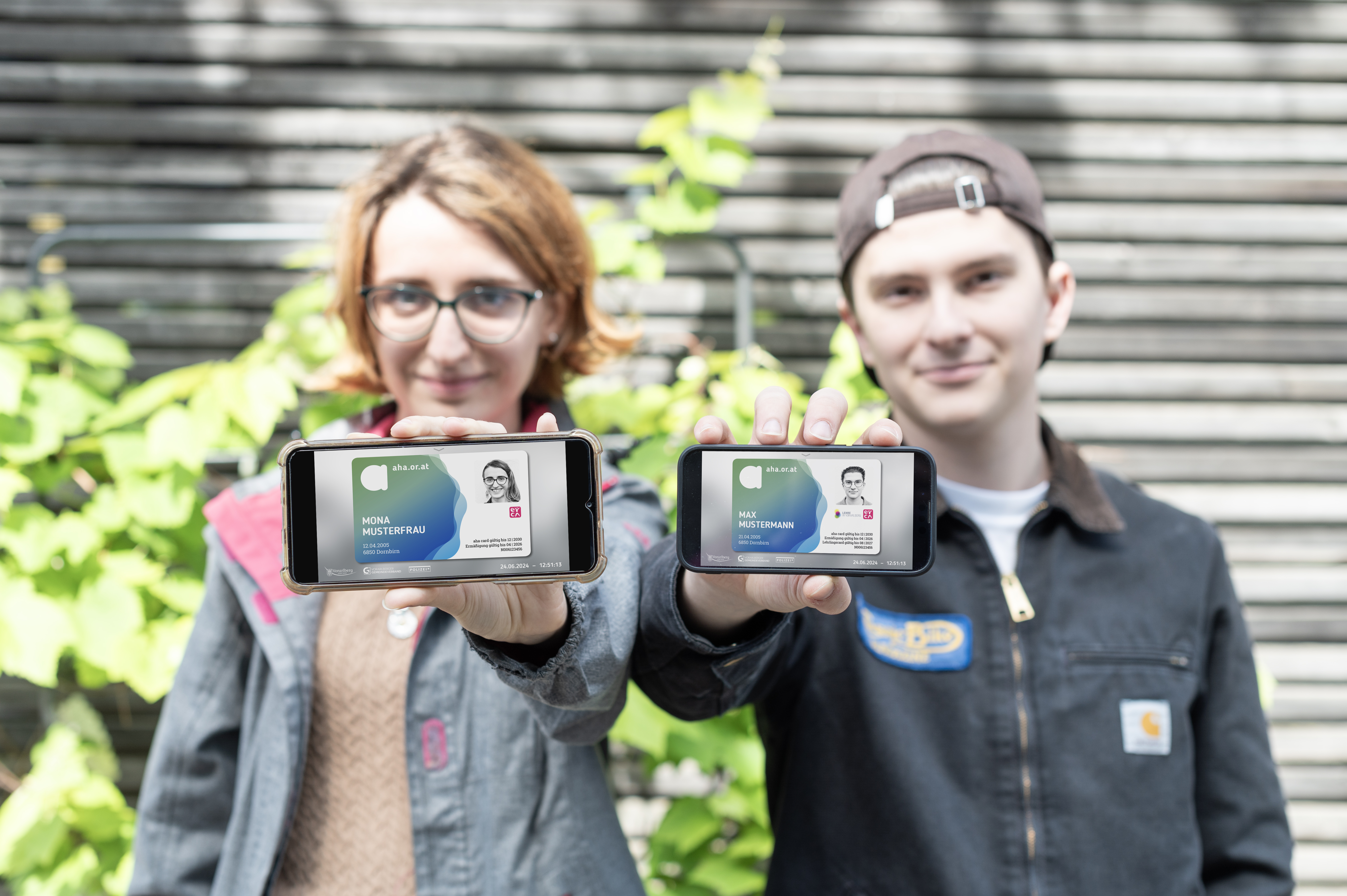 Zwei Personen halten Smartphones mit digitalen Ausweisen vor einem grünen Hintergrund in der Hand.