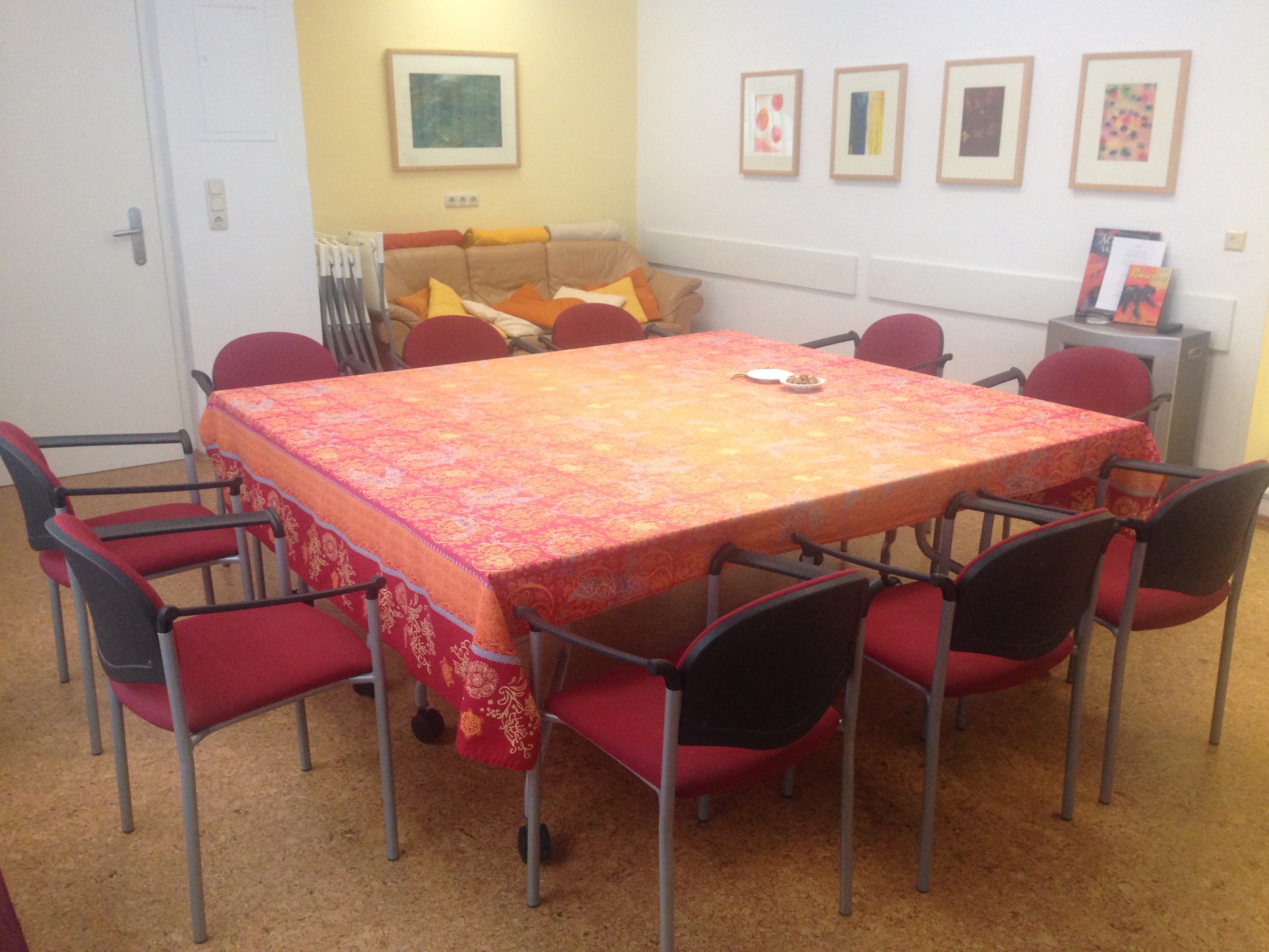 Ein Konferenzraum mit einem großen Tisch, umgeben von Stühlen, und dekorativen Bildern an der Wand.
