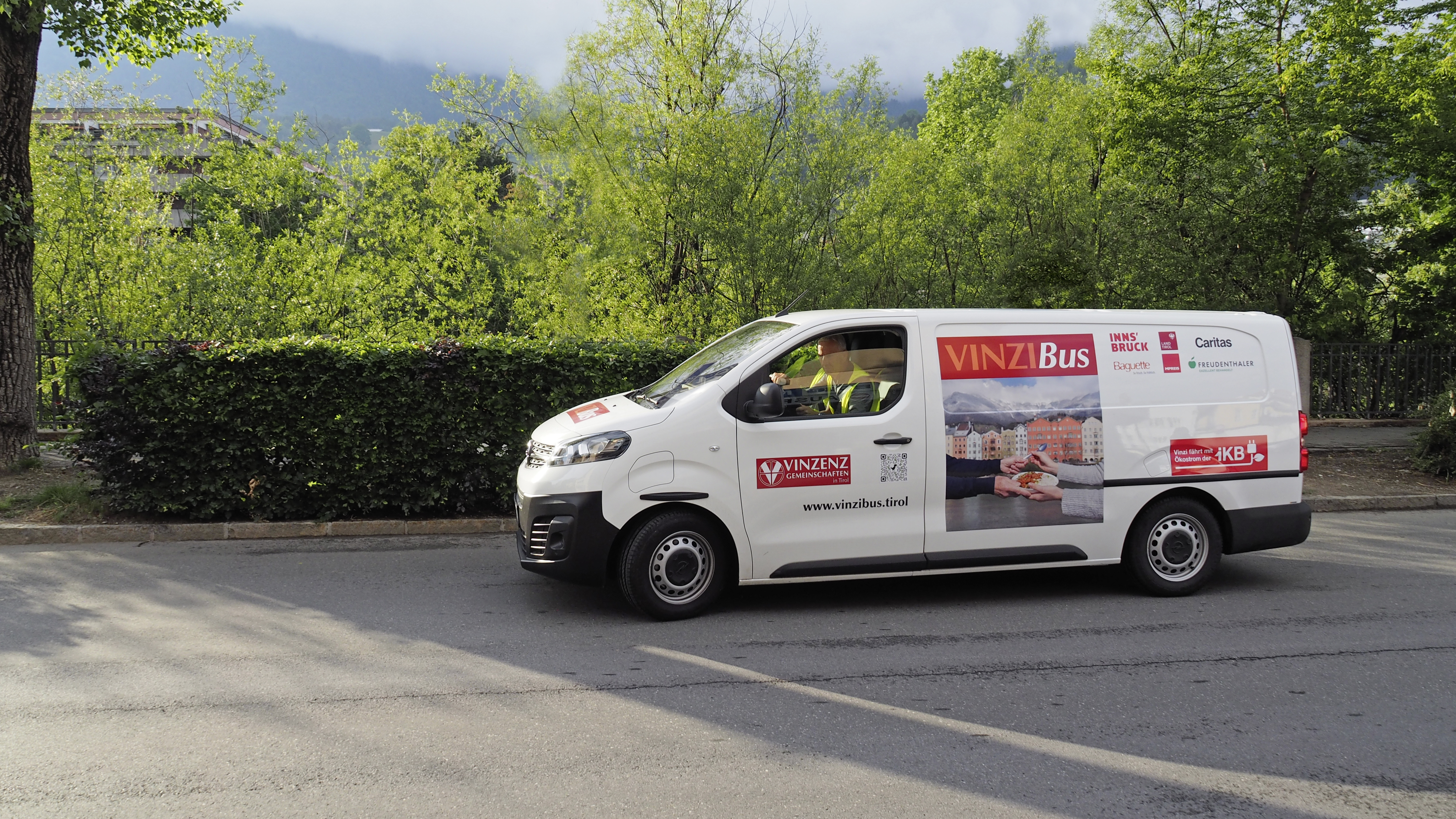 Ein Lieferwagen mit Werbung für "VINZ Bus" fährt an einer grünen Landschaft entlang.