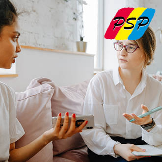 Zwei Frauen diskutieren in einem hellen Raum, eine zeigt ihr Handy, die andere hört aufmerksam zu.