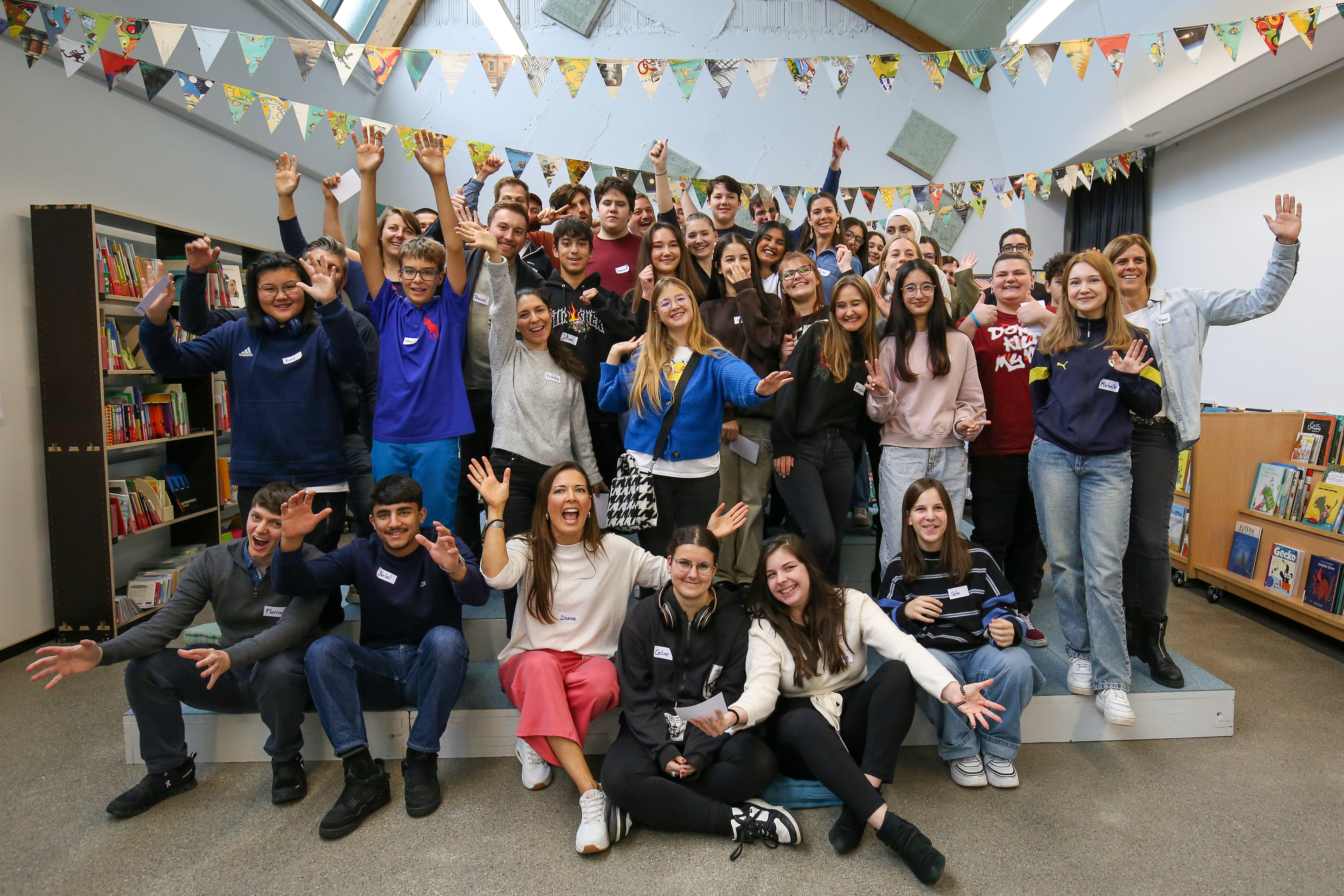 Gruppenselfie von 40 jungen Menschen in einem hellen Raum, alle lächeln und posieren fröhlich zusammen.