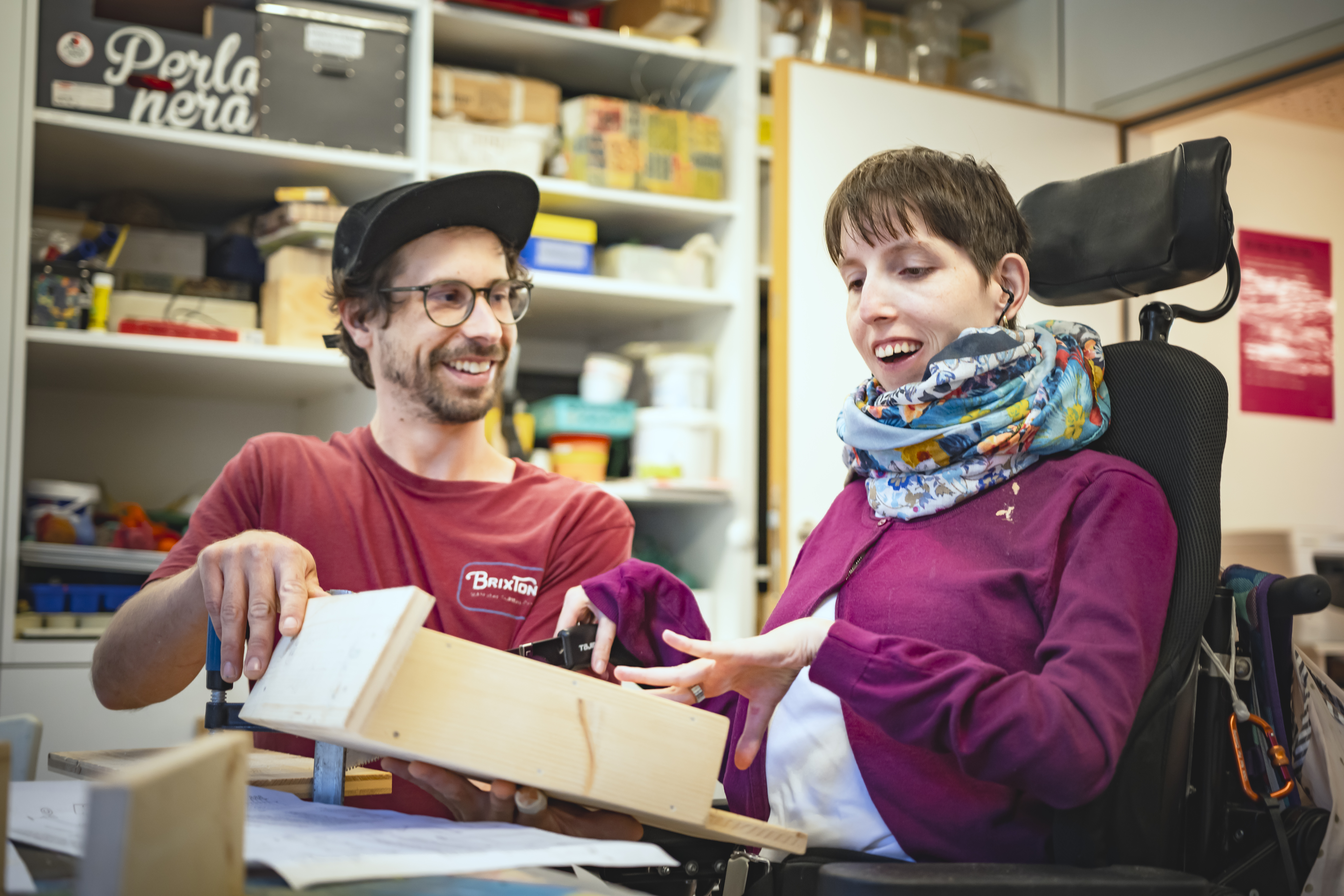 Ein Mann und eine Frau im Rollstuhl arbeiten gemeinsam an einem Holzprojekt in einer Werkstatt.